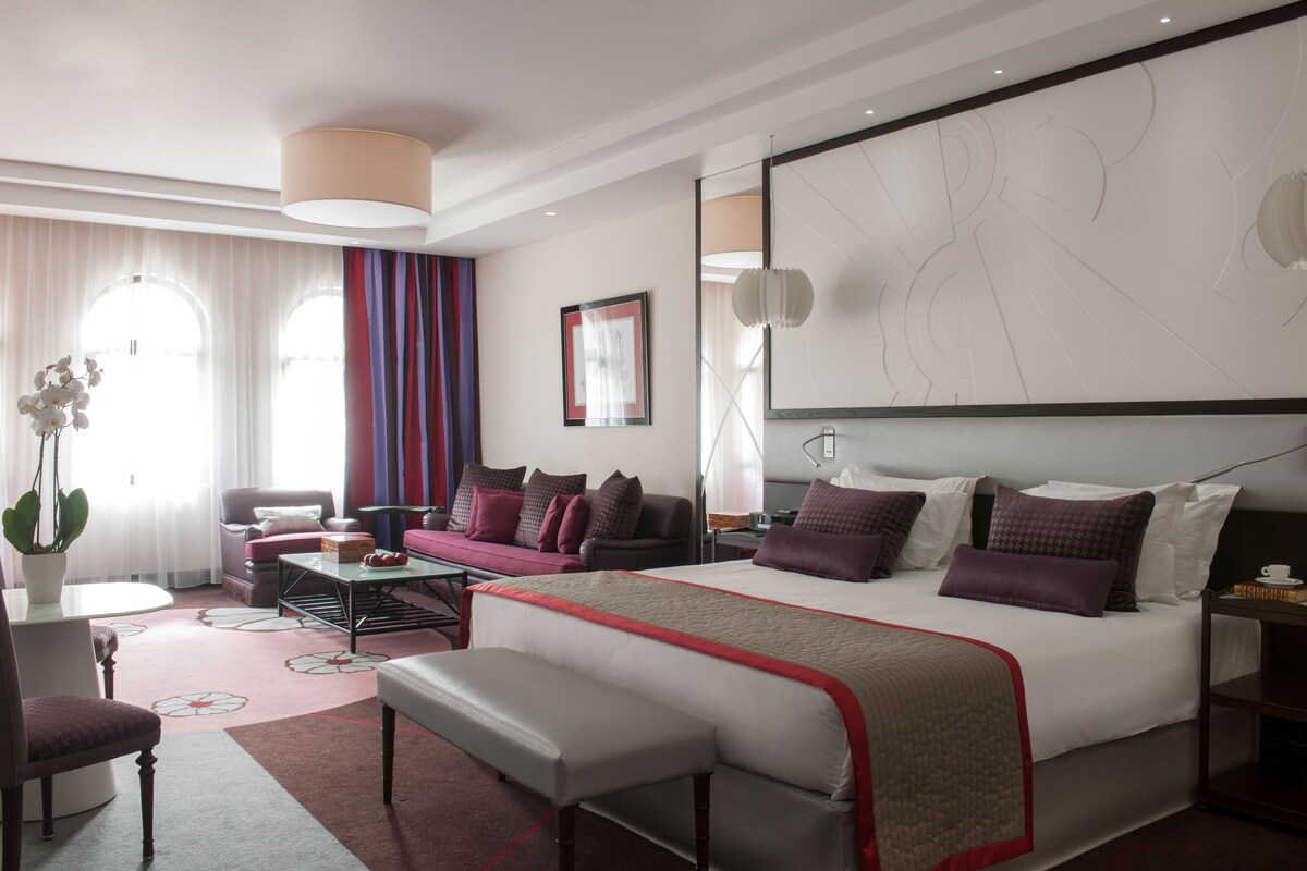 Una habitación de hotel moderna con una cama grande, un sofá, un escritorio y una planta en maceta.