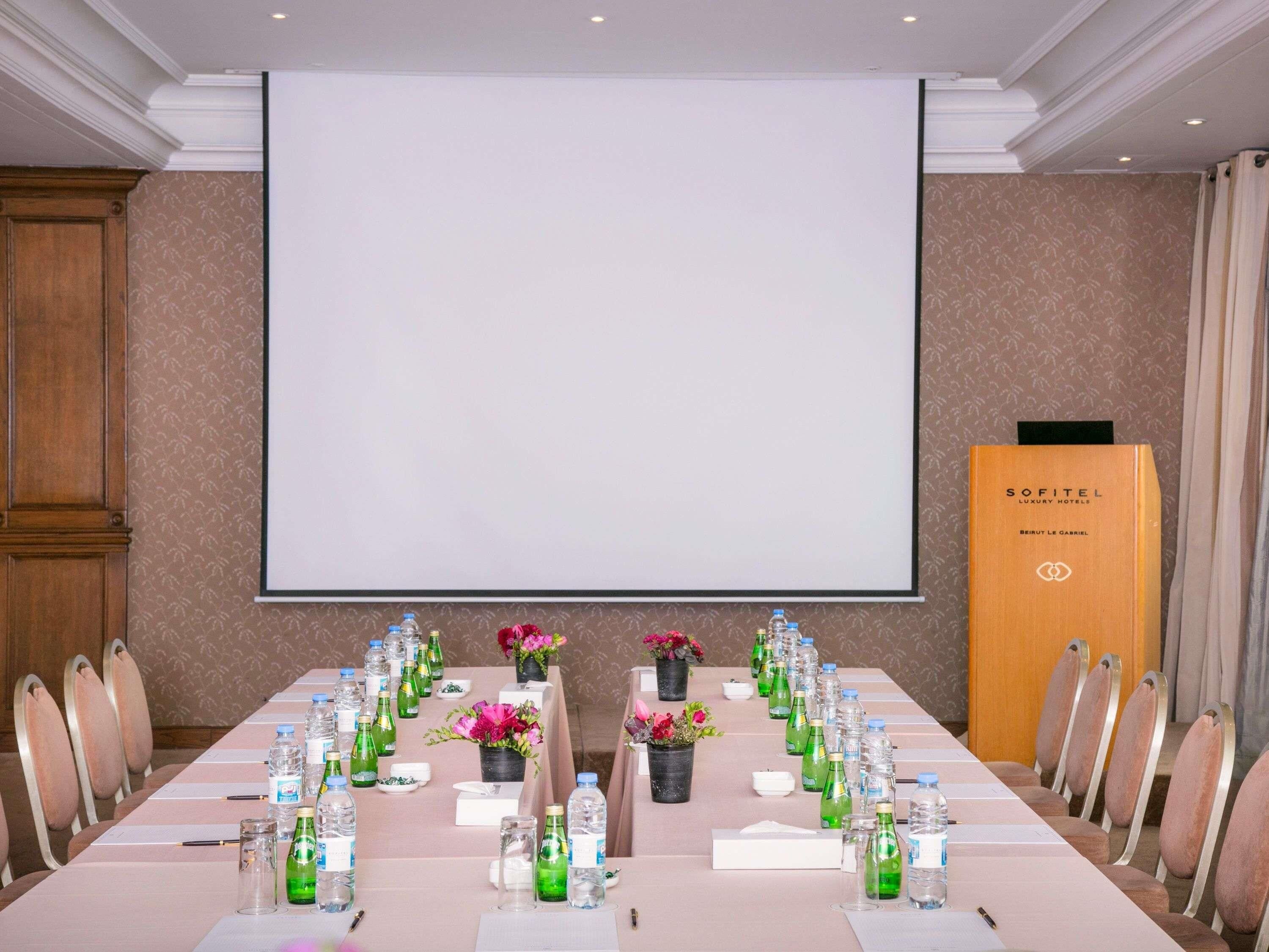 A conference room with a long table, chairs, a projector screen, and a podium.