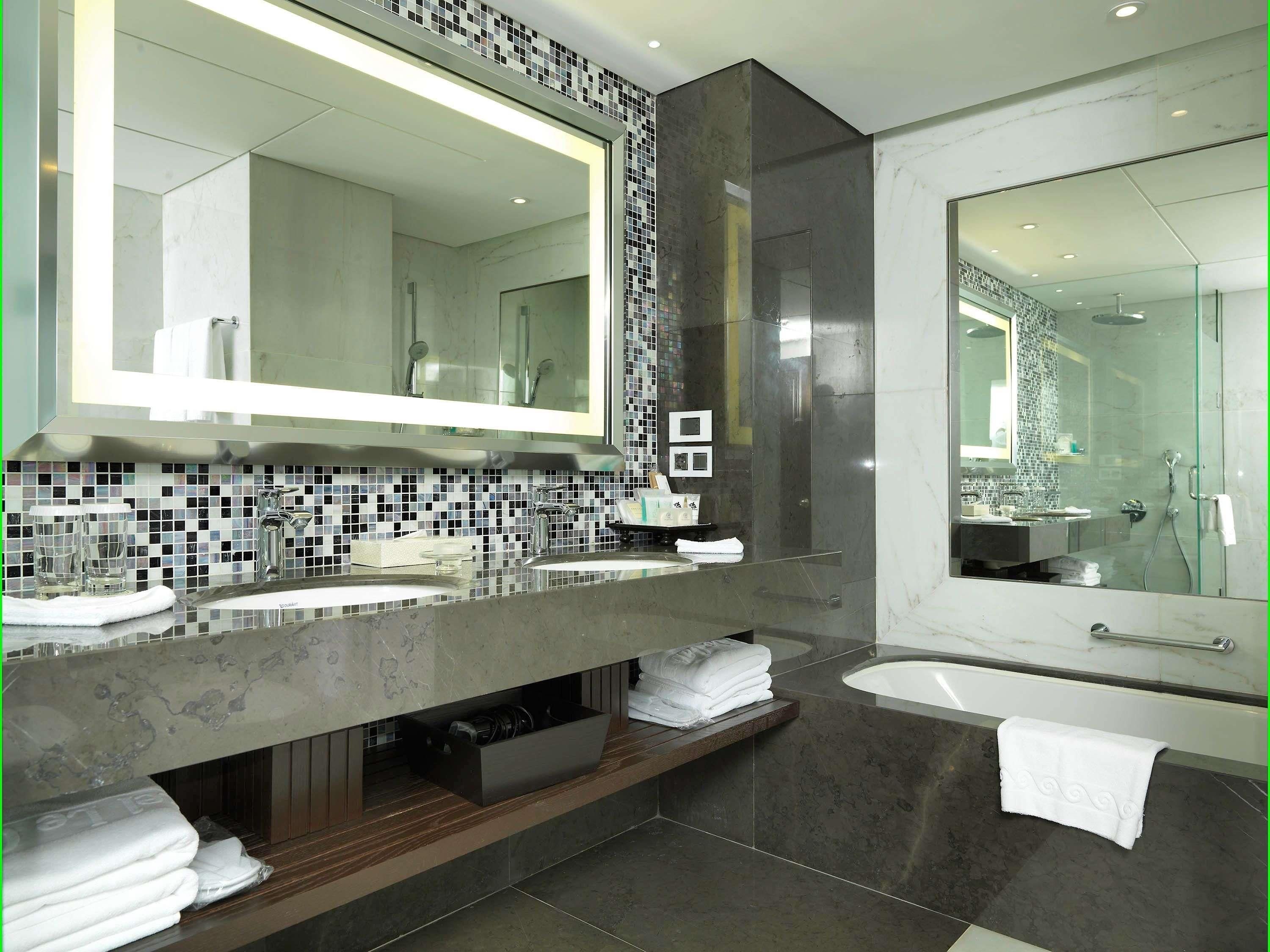 A modern bathroom with a large mirror, two sinks, a shower, and a vanity with a tiled backsplash.