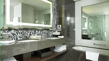 A modern bathroom with a large mirror, two sinks, a shower, and a vanity with a tiled backsplash.
