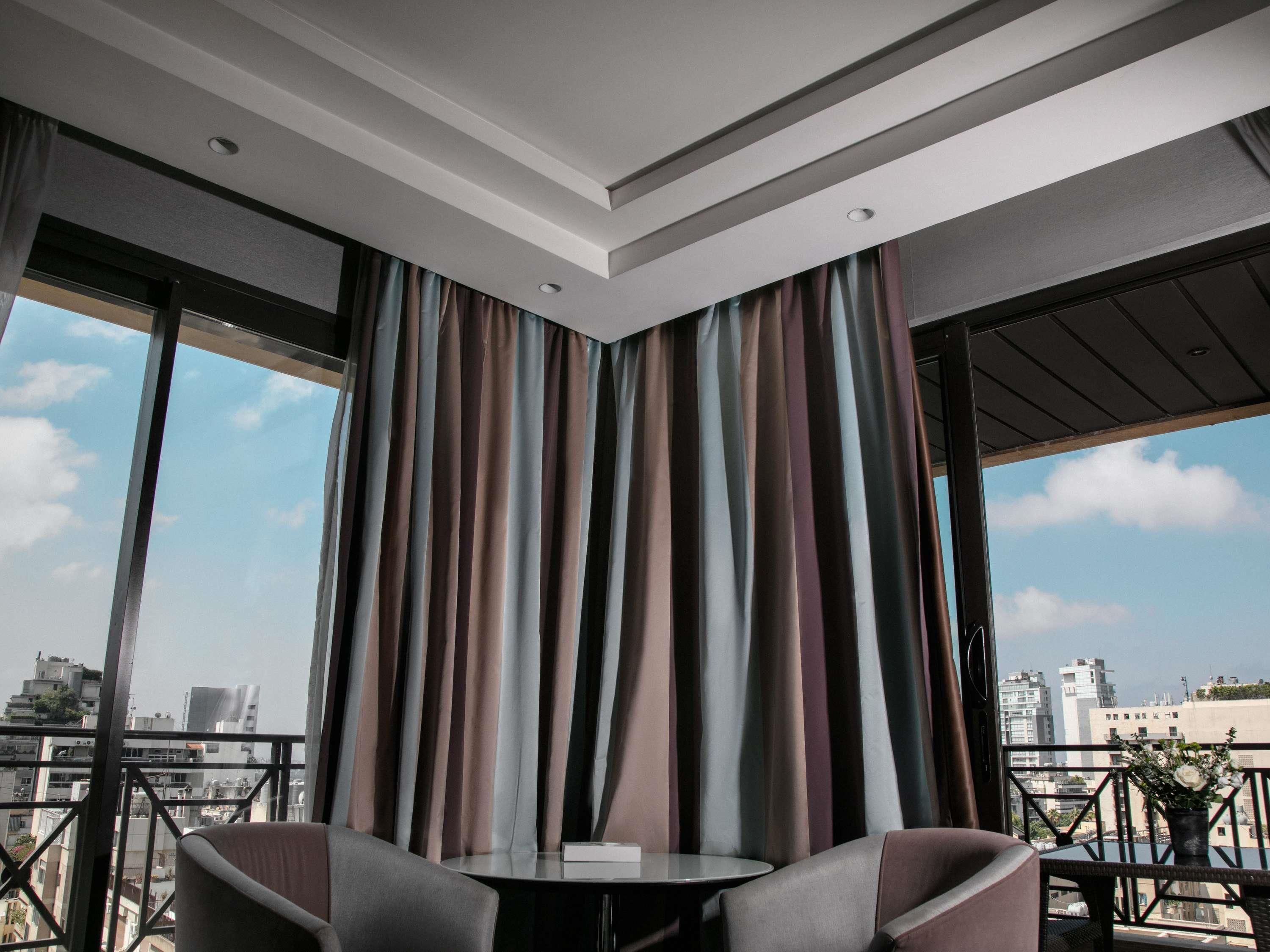 A modern room with a round table and two chairs, large windows with curtains, and a view of the cityscape.