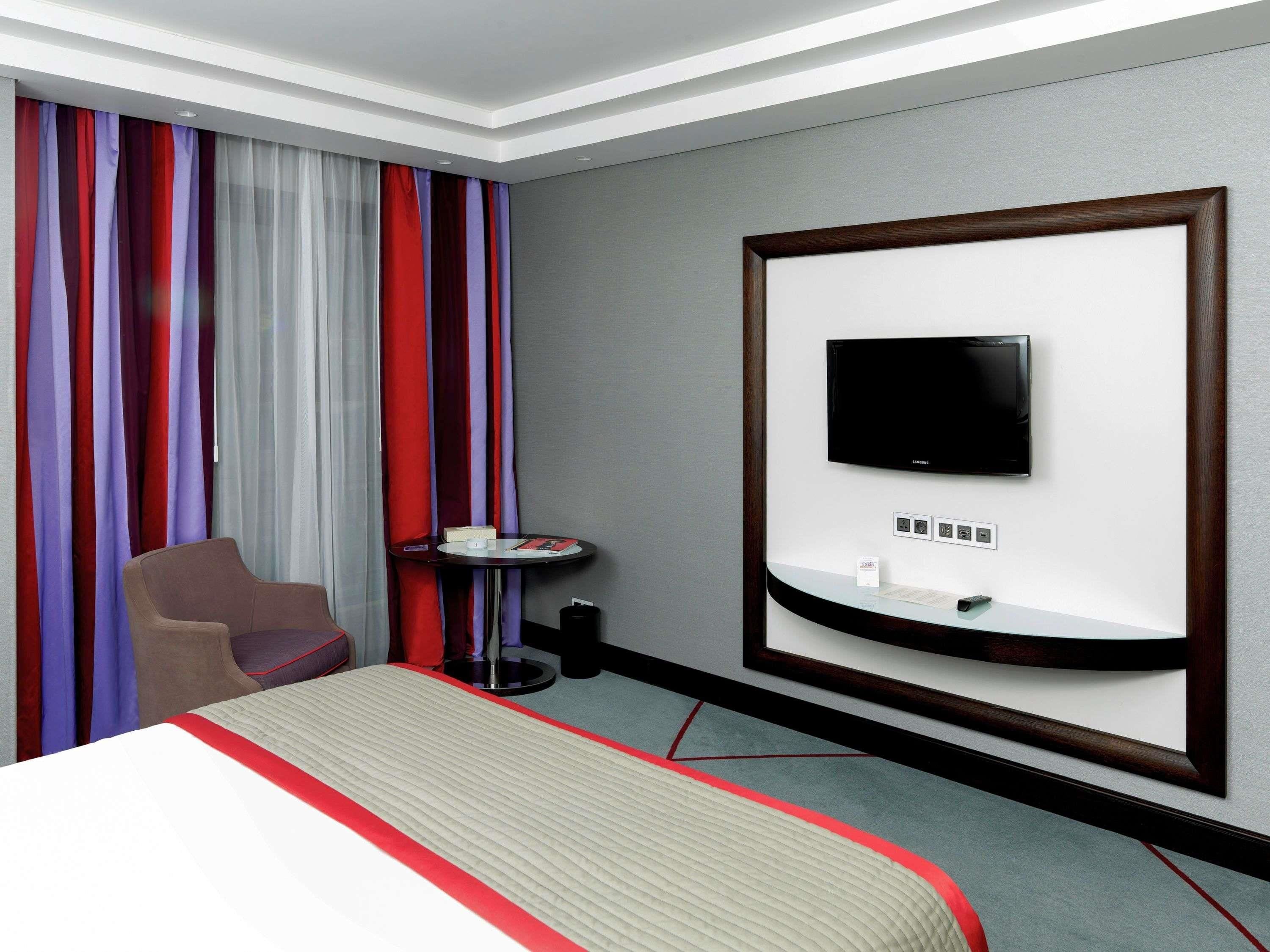 Habitación de hotel con una cama, televisión montada en la pared, una mesita y una silla.