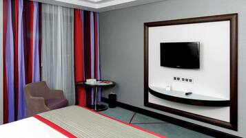 A hotel room with a bed, a TV mounted on the wall, a small table, and a chair.