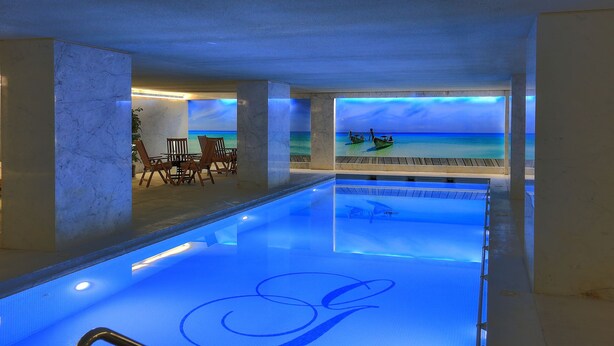 Une piscine avec vue sur une plage et des bateaux, entourée de colonnes de marbre et agrémentée d’un espace détente.