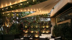 Un espace de restauration en plein air avec des tables et des chaises, un mur recouvert de plantes suspendues et une marquise au-dessus.