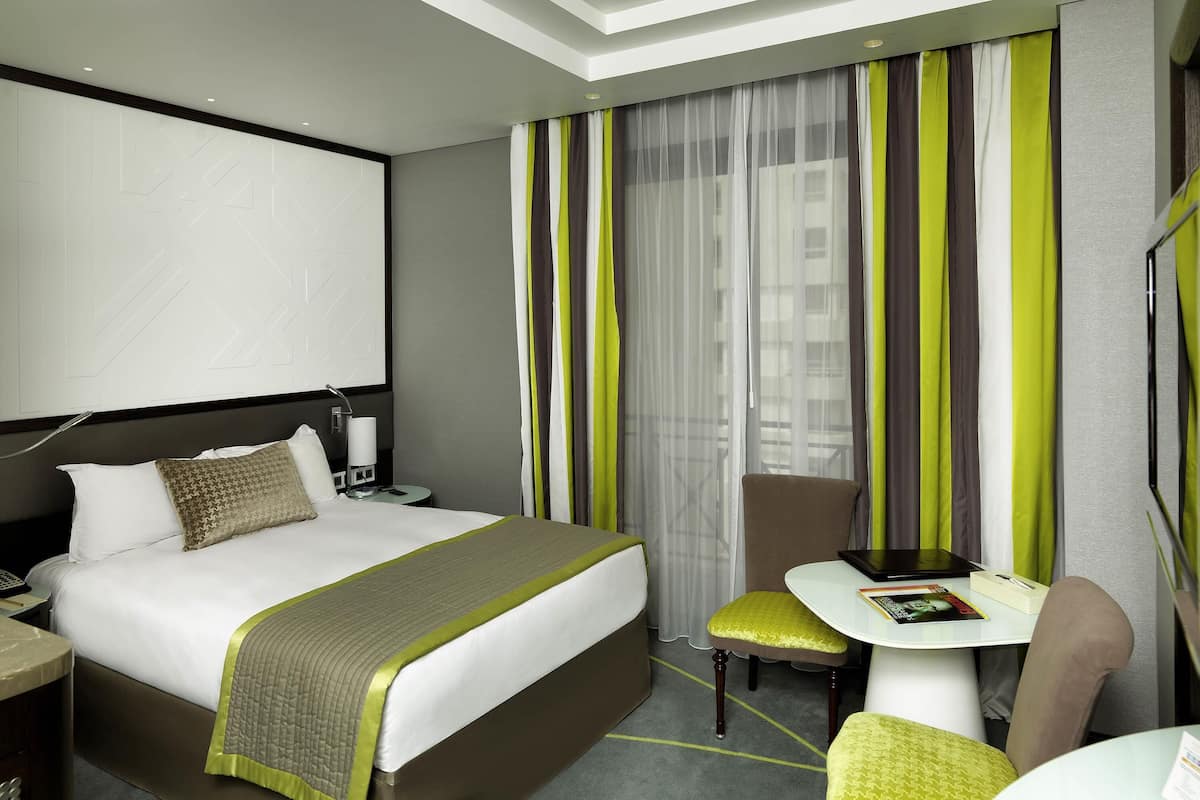 Una habitación de hotel con cama, mesita de noche, silla y una pequeña mesa con otra silla.