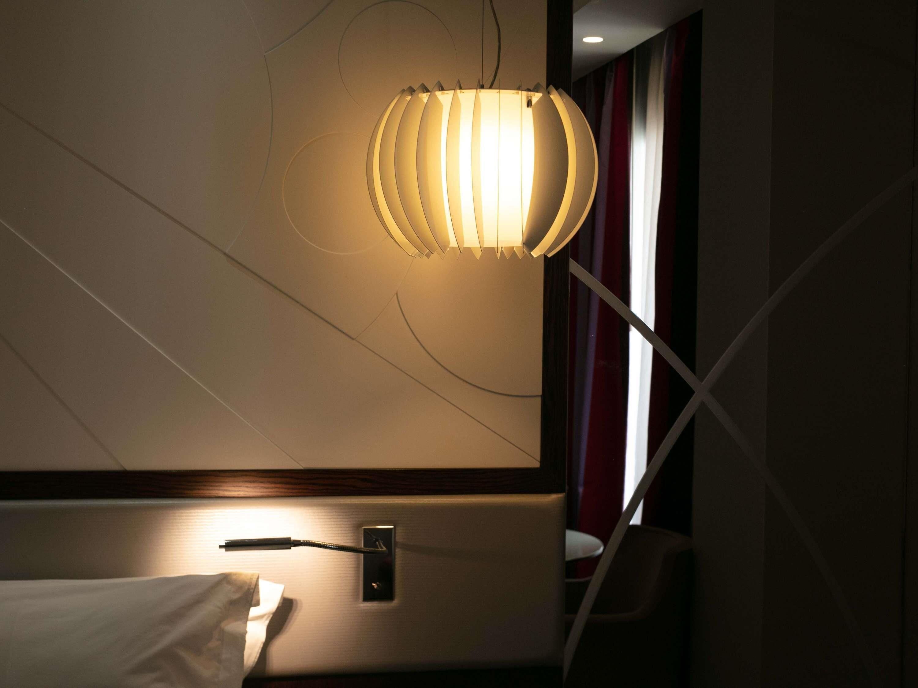 A hotel room with a bed, a bedside table, a lamp, and a window with curtains.