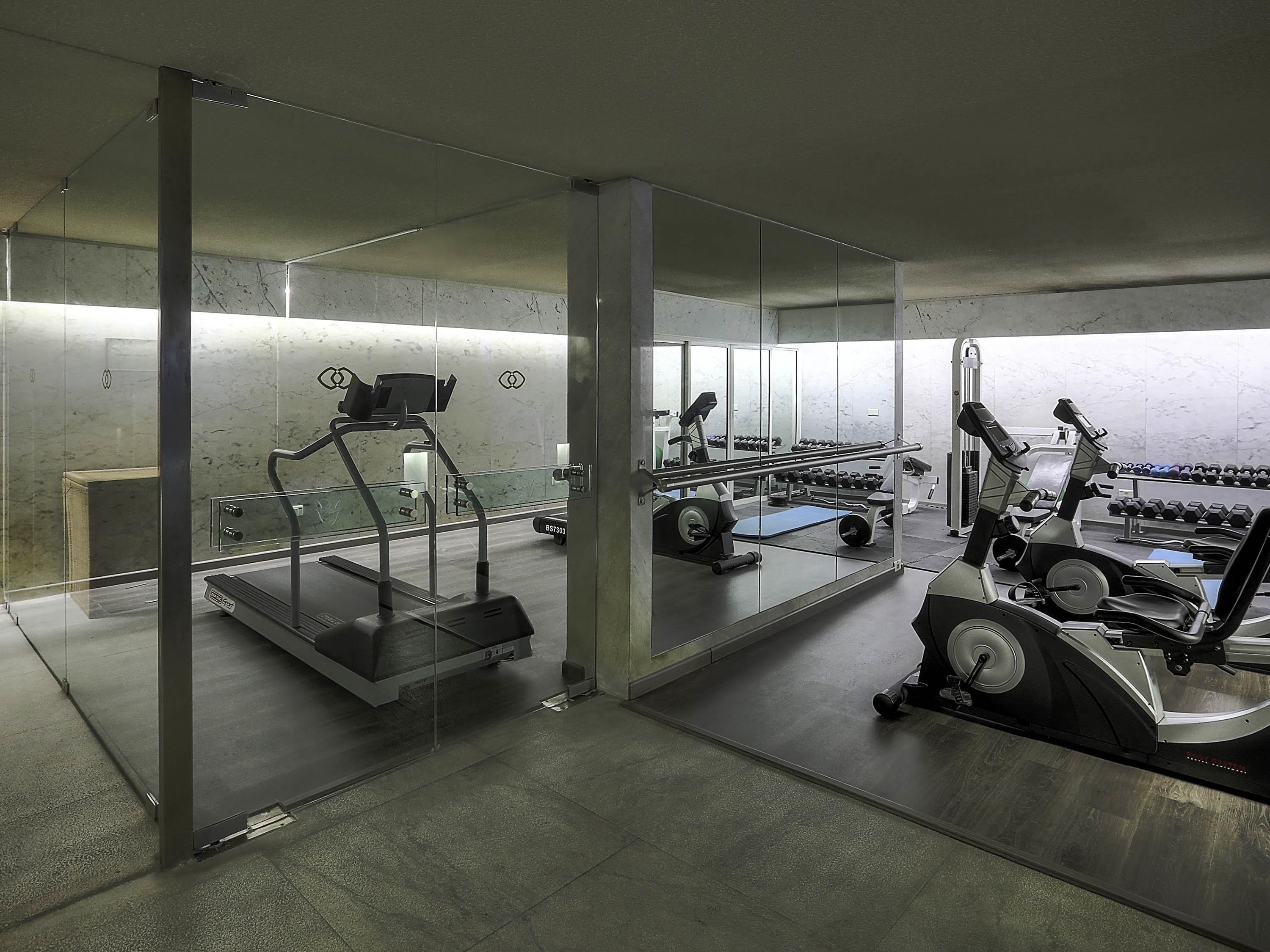 A gym with exercise equipment, a mirrored wall, and a concrete floor.