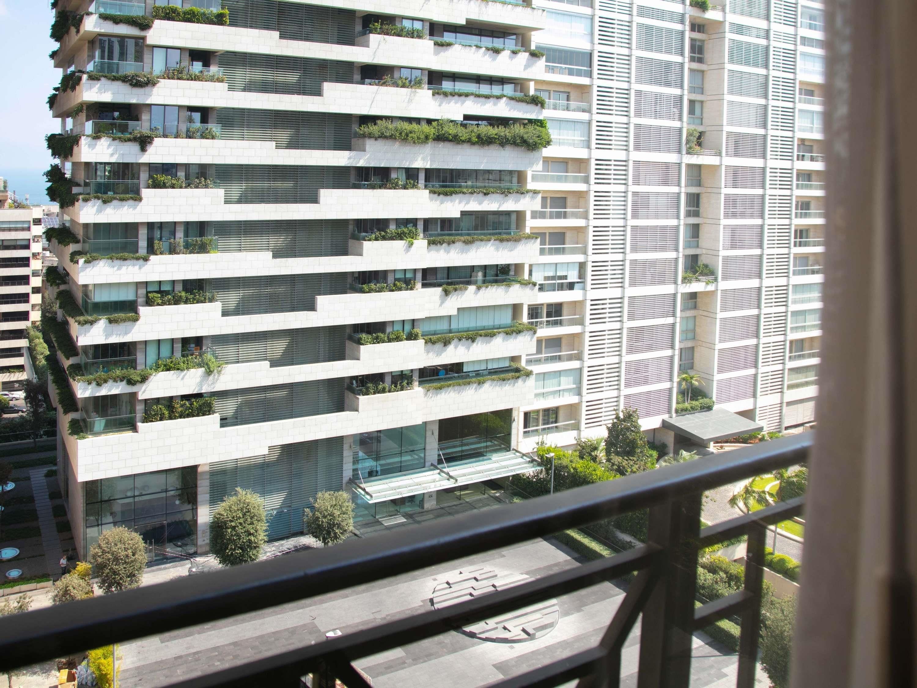 A modern high-rise building with multiple balconies, large windows, and a glass entrance.