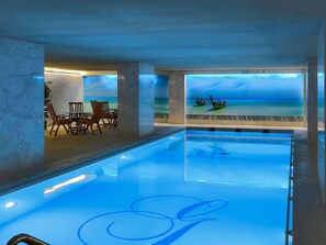 Una piscina con vista al océano y barcos, rodeada de columnas de mármol y sillas de madera.