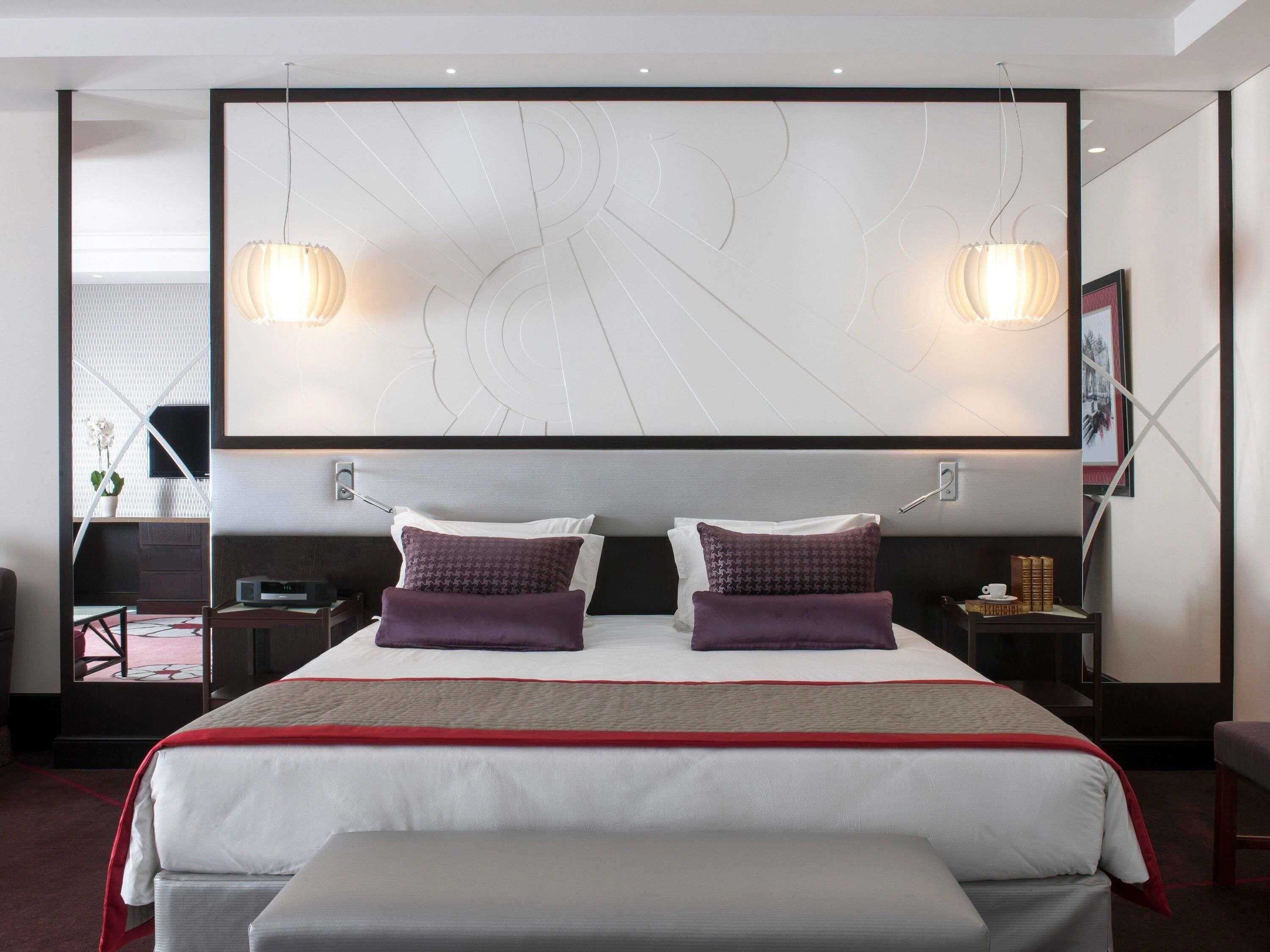 Una habitación de hotel moderna con una cama grande, dos lámparas de noche, un televisor de pantalla plana y una mesita de noche con una taza y libros.