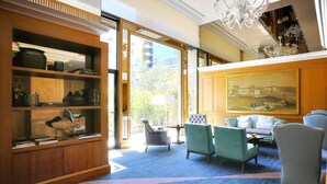 Un hall d’hôtel doté d’une grande bibliothèque, d’un espace salon, d’un lustre et d’un tableau accroché au mur.