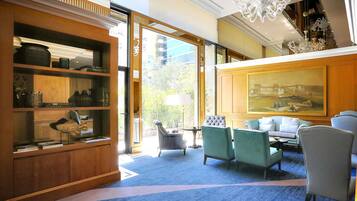 A hotel lobby with a large bookshelf, seating area, chandelier, and a painting on the wall.