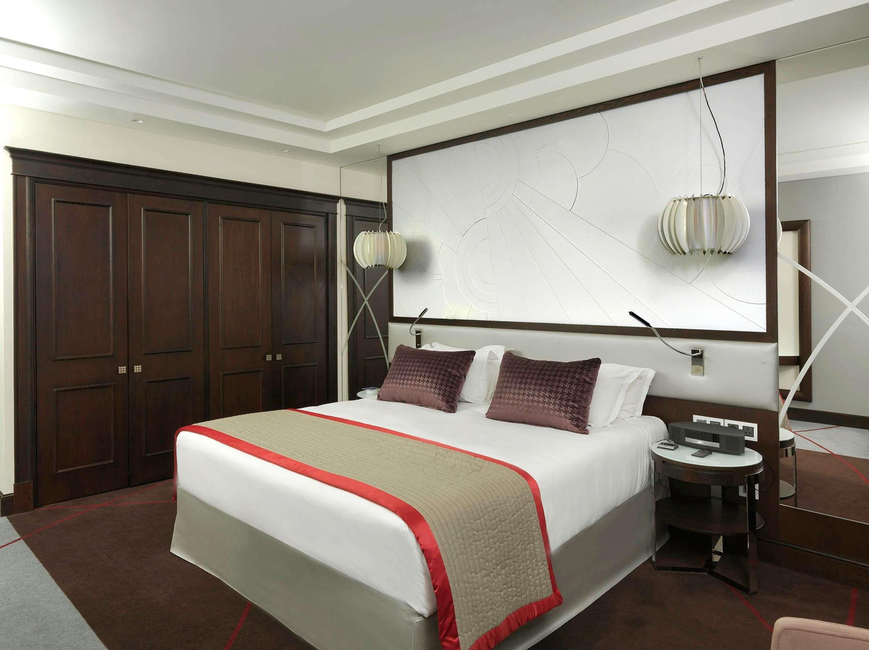 A hotel room with a large bed, a desk, a chair, a wardrobe, and a wall-mounted artwork.