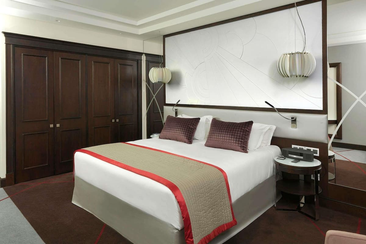 Habitación de hotel con una cama grande, un escritorio, una silla, un armario y una obra de arte colgada en la pared.