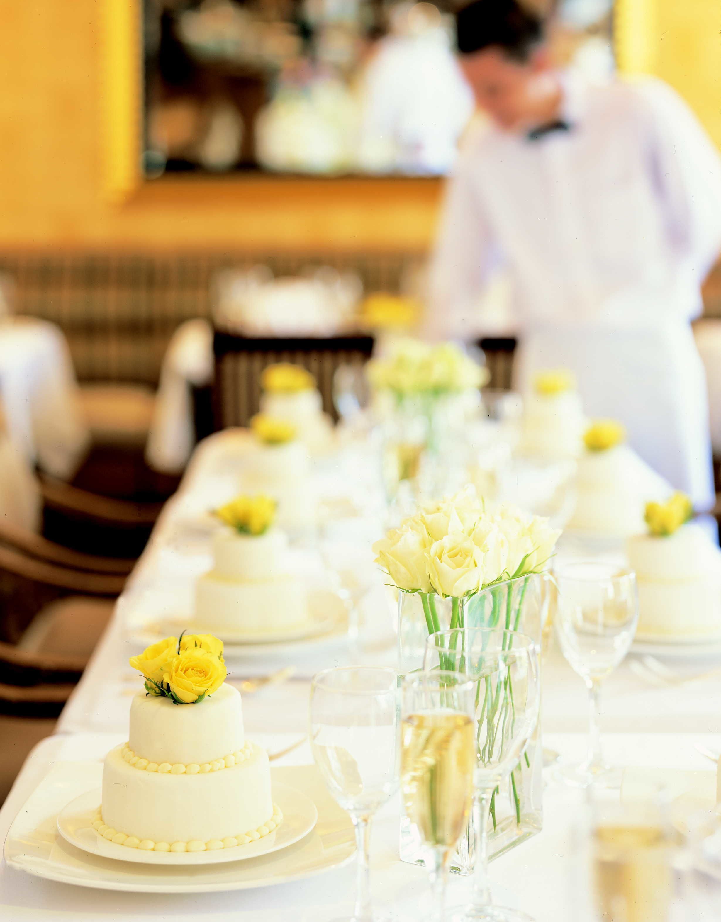 Een lange eettafel met witte tafelkleden, voorzien van glazen servies en witte borden.
