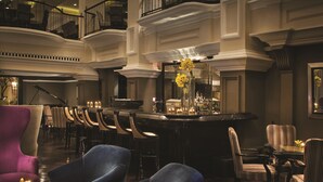 Een ruime lobby met een statige trap, meerdere zithoeken en een bar met een piano.