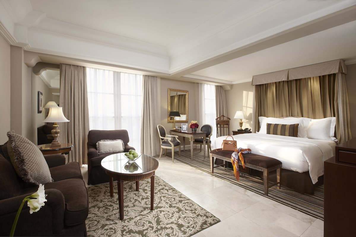 A hotel room with a bed, a sofa, a dining table, and a desk.