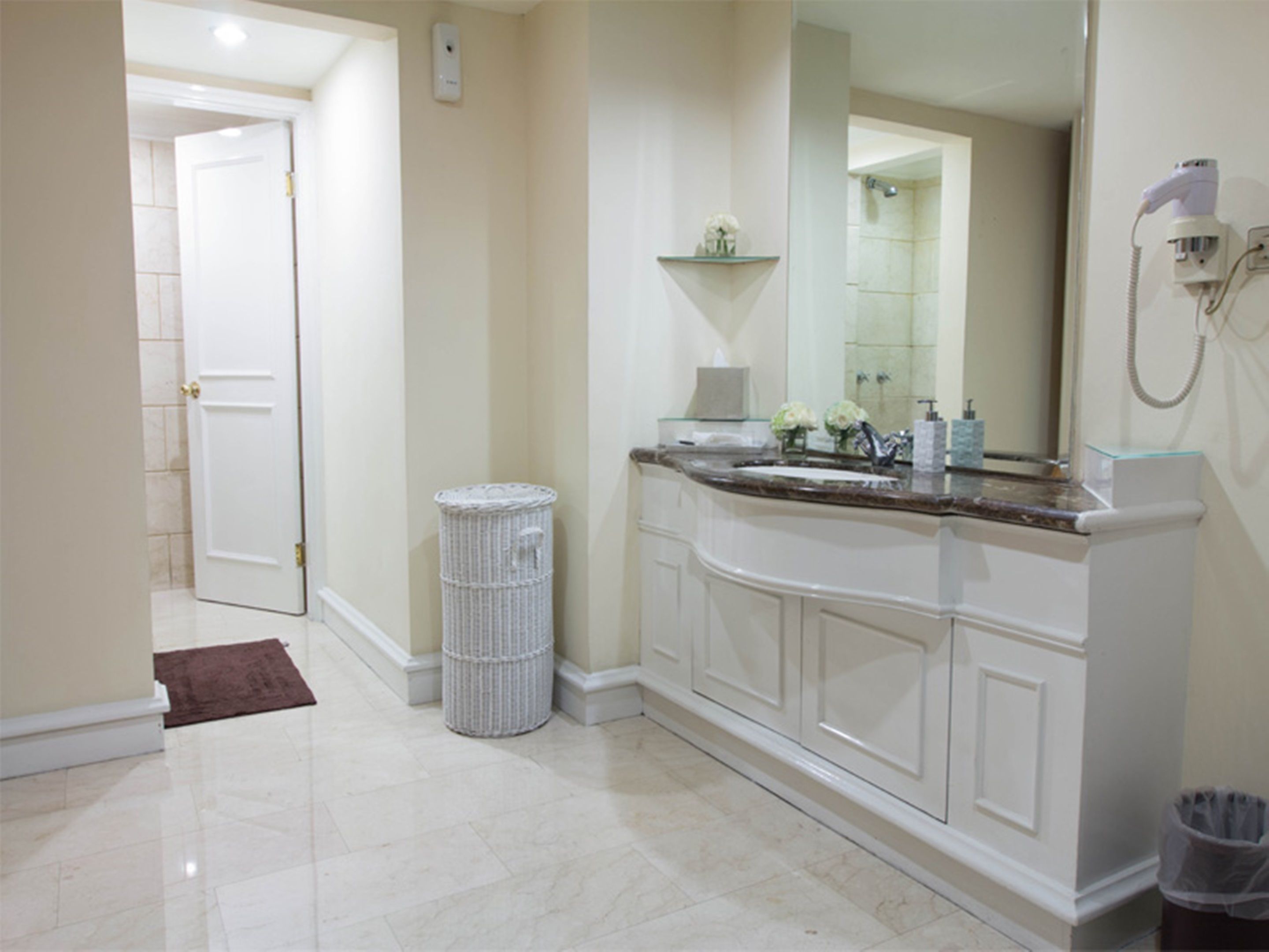 A bathroom with a marble floor, a white vanity with a sink, a mirror, and a shower area.