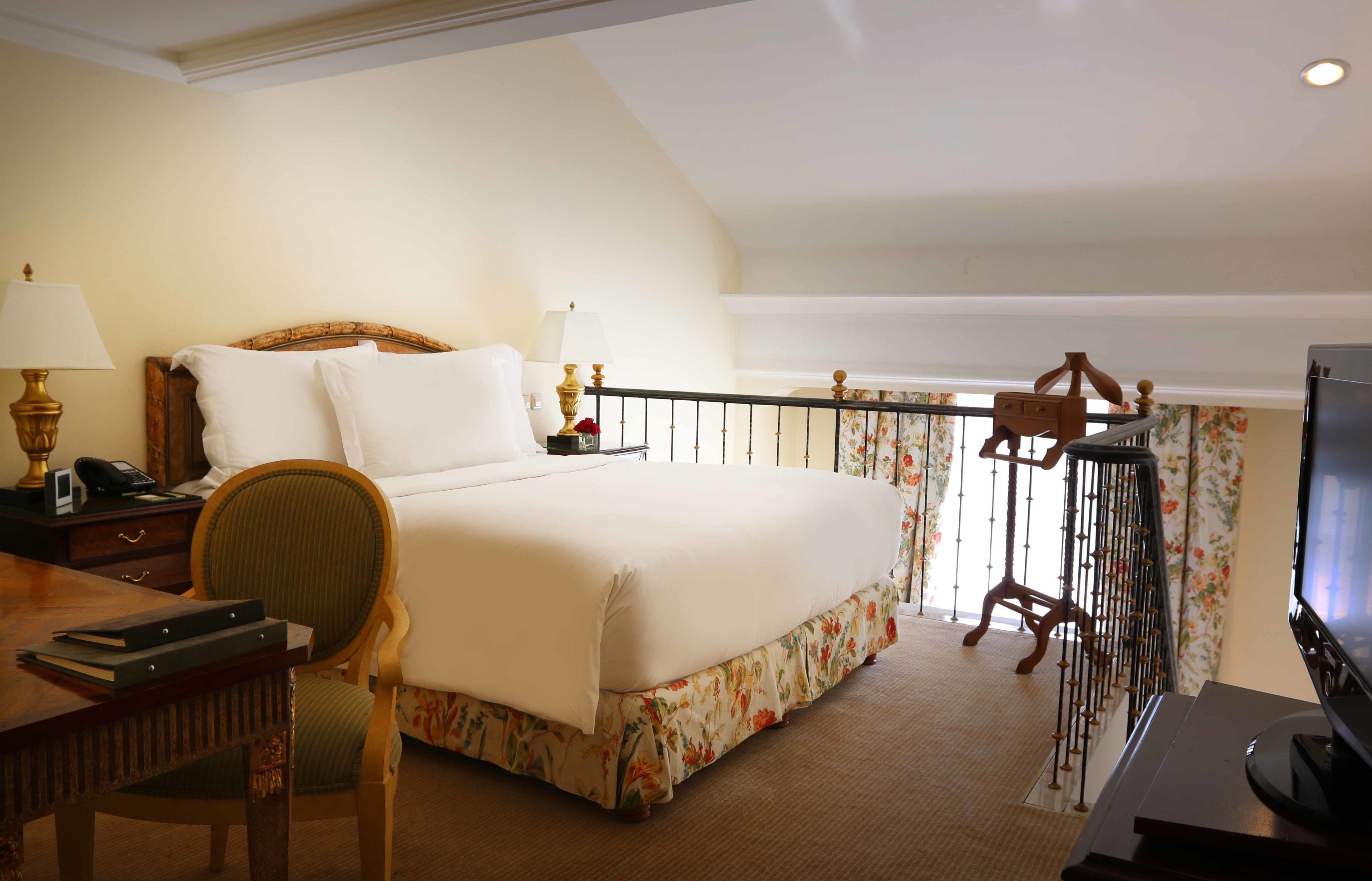 Une chambre d’hôtel comprenant un lit, un bureau avec une lampe, une chaise, un téléviseur et un balcon avec une balustrade.