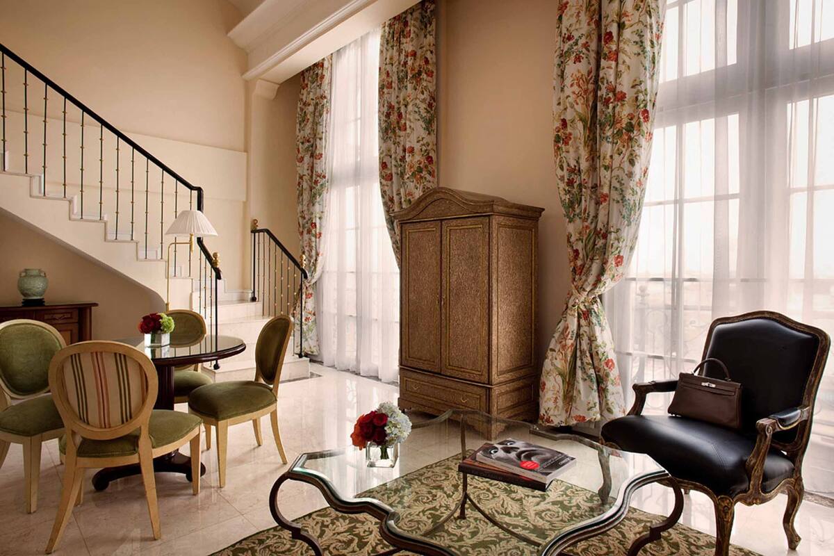 A spacious living room with a staircase, a wooden cabinet, and a black leather chair.