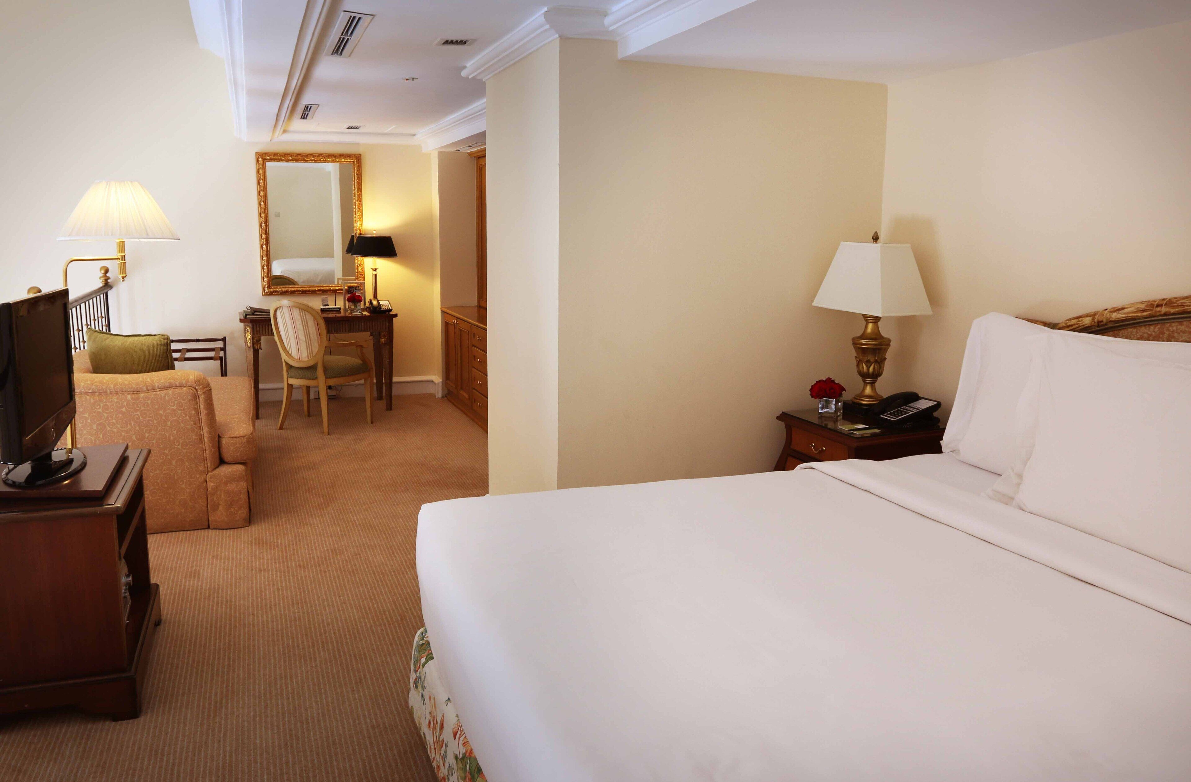 Una habitación de hotel con una cama grande, un escritorio con una silla, un televisor y una lámpara.