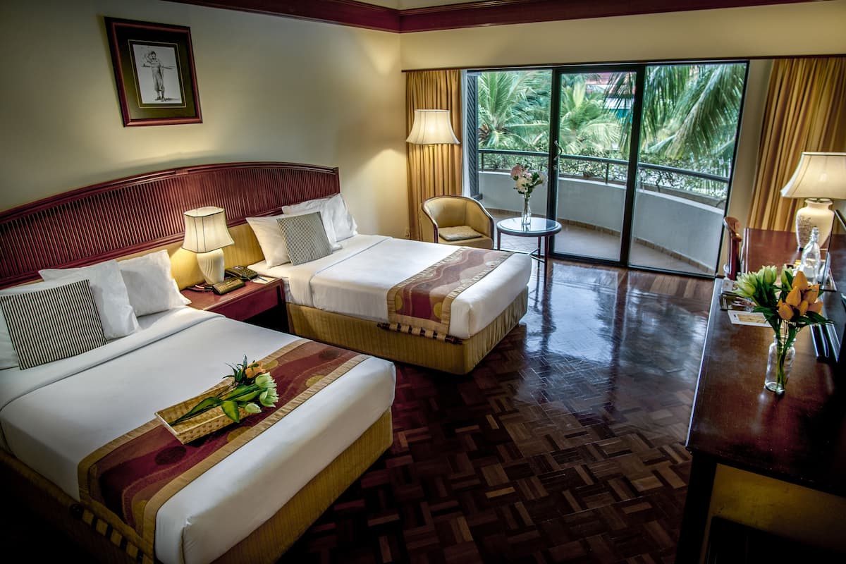 A hotel room with two beds, a small table, a chair, and a view of the outdoors.