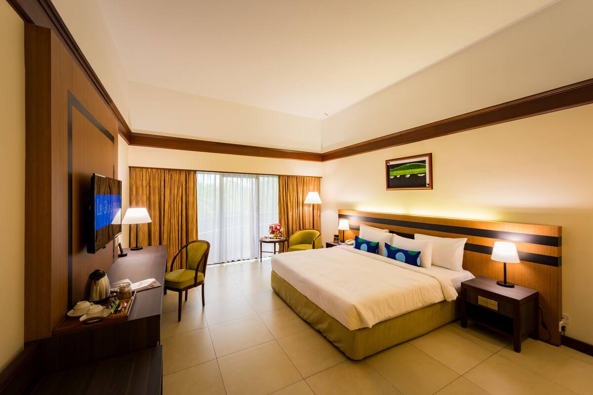 A hotel room with a large bed, a desk with a chair, a TV, and a nightstand with a lamp.