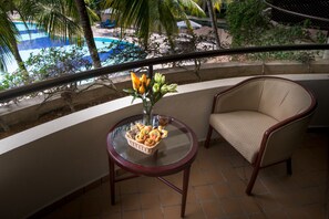 Un balcon avec un fauteuil en osier, une table en verre sur laquelle se trouve un panier de viennoiseries et un vase rempli de fleurs.