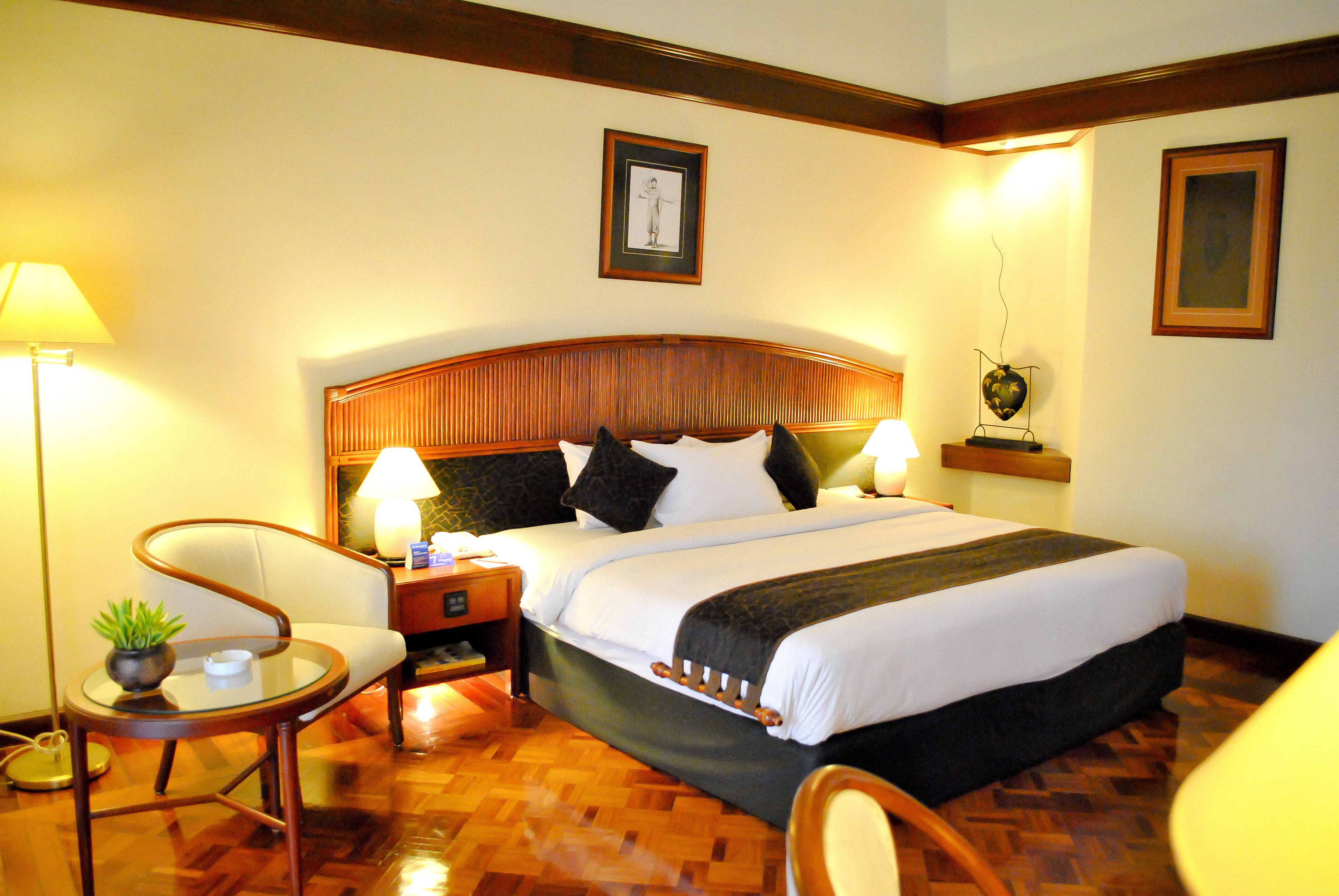 A hotel room with a large bed, two bedside tables with lamps, a chair, and a small table with a plant.
