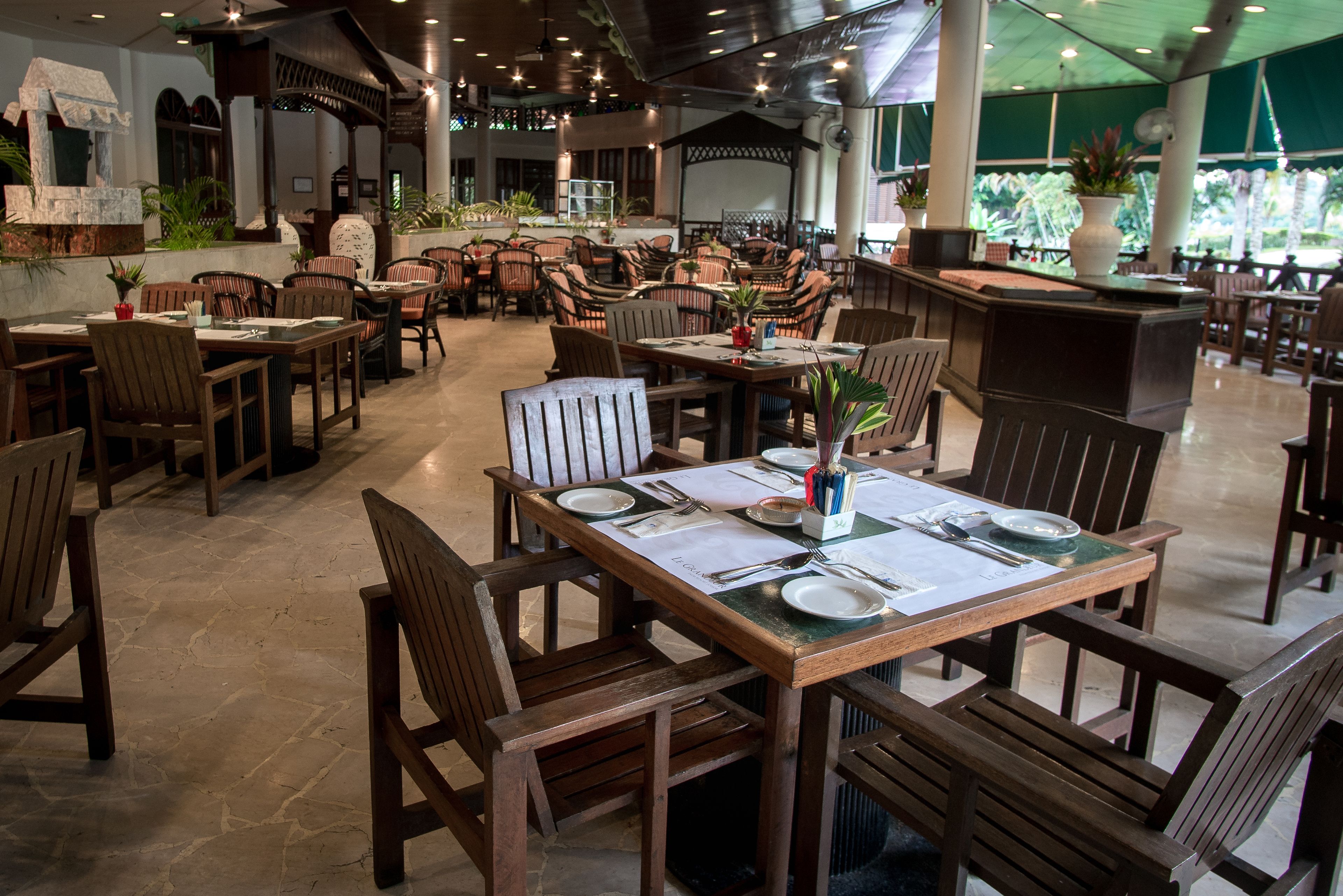 Un restaurant spacieux avec des tables et des chaises en bois, un coin bar et des plantes en pot.