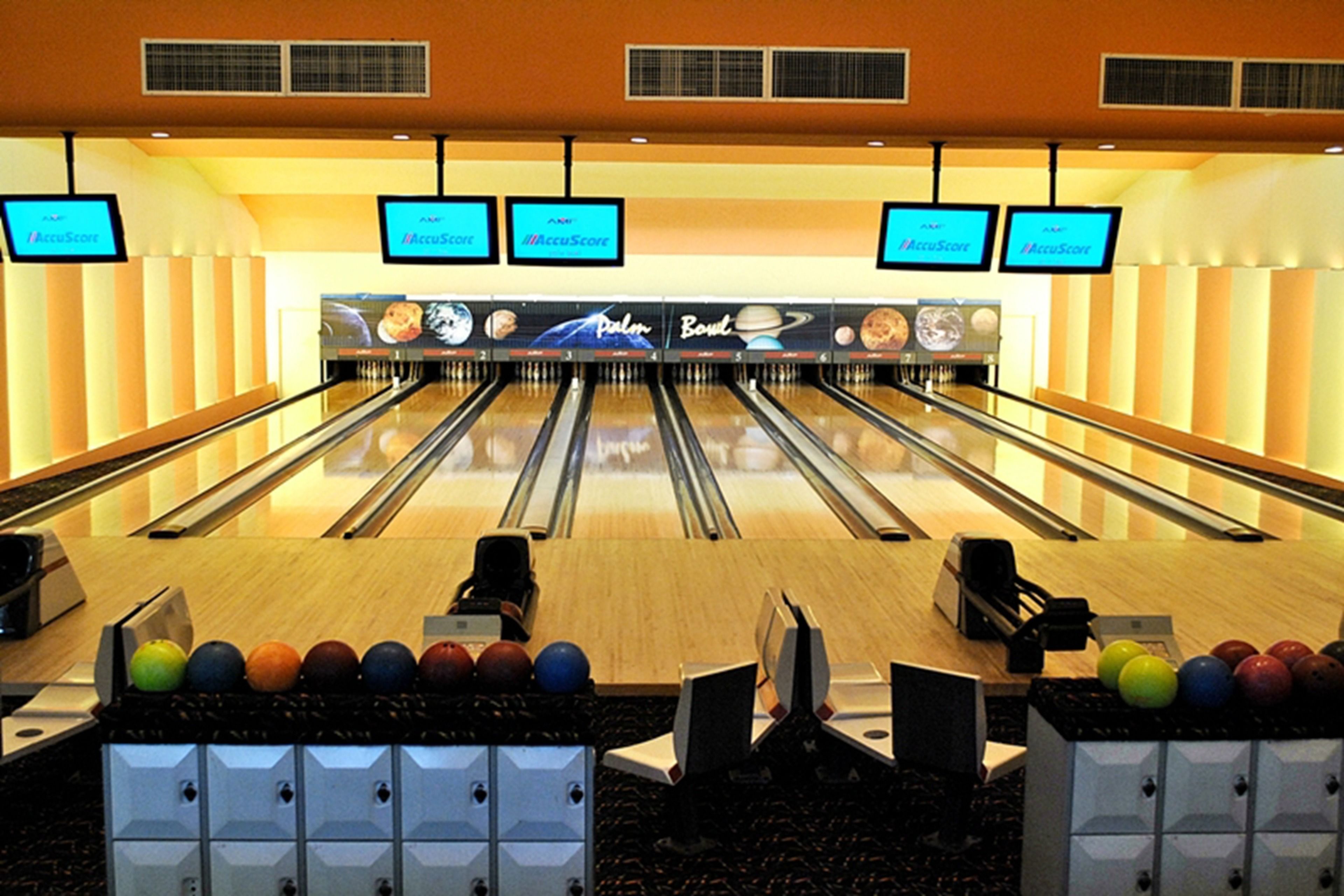 A bowling alley with multiple lanes, a scoreboard, and a row of bowling balls.