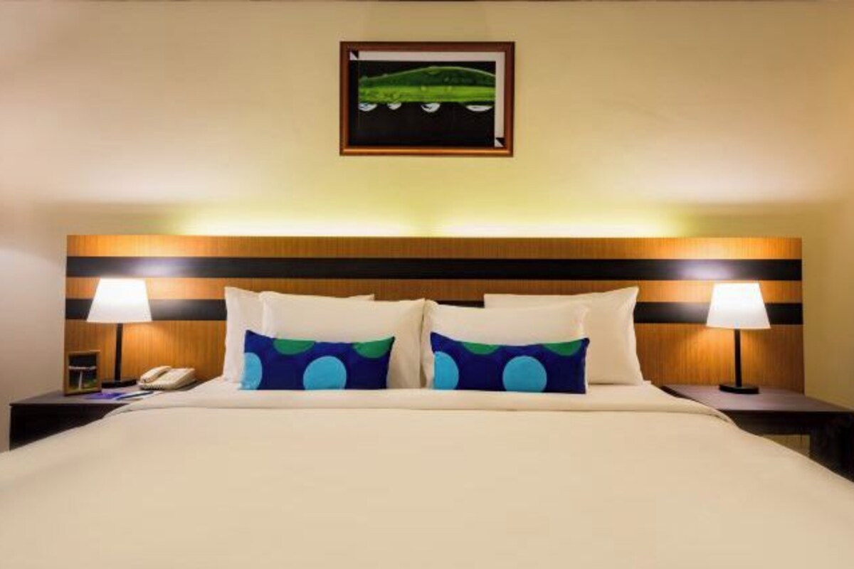 A hotel room with a bed, two bedside tables, a telephone, and a painting on the wall.