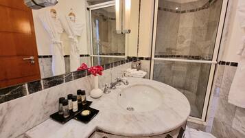 A bathroom with a marble sink, a glass shower enclosure, and a mirror reflecting a robe and a flower.