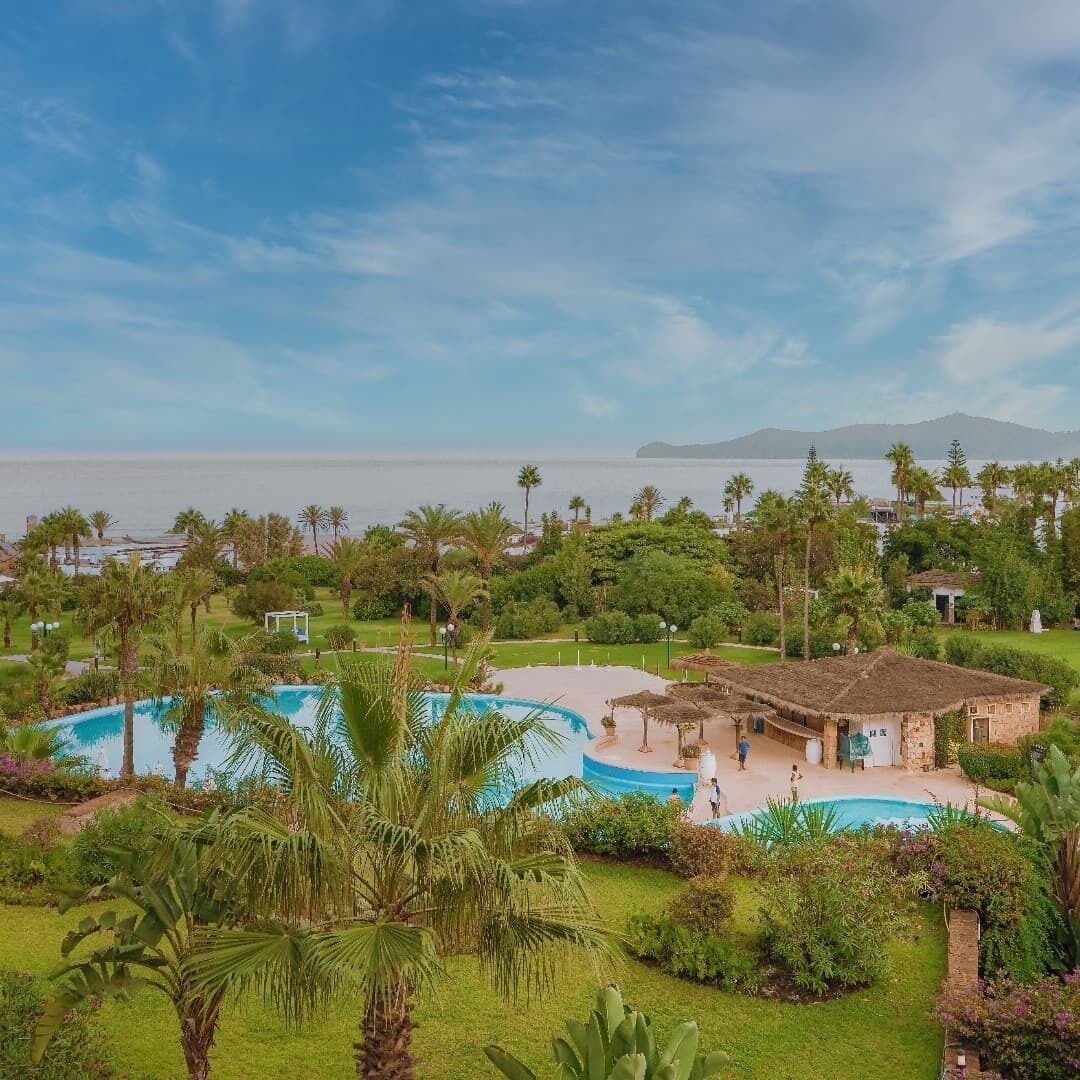 Un complex turístic amb una piscina gran, vegetació exuberant i vistes a l'oceà.