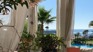 A sunlit room with a view of the sea, featuring a sofa, a wooden table, and various plants. - Marina Smir Hotel & Spa (Allyene)