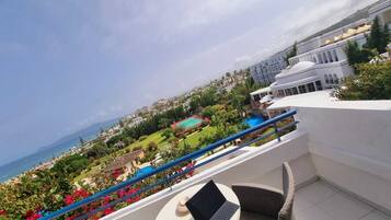 Un balcón con una laptop sobre una mesa, con vista a una piscina y al mar, además de edificios.