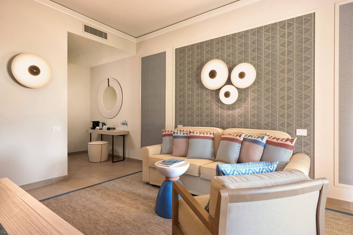 A modern hotel room with a sofa, a coffee table, a small round table, and a mirror.