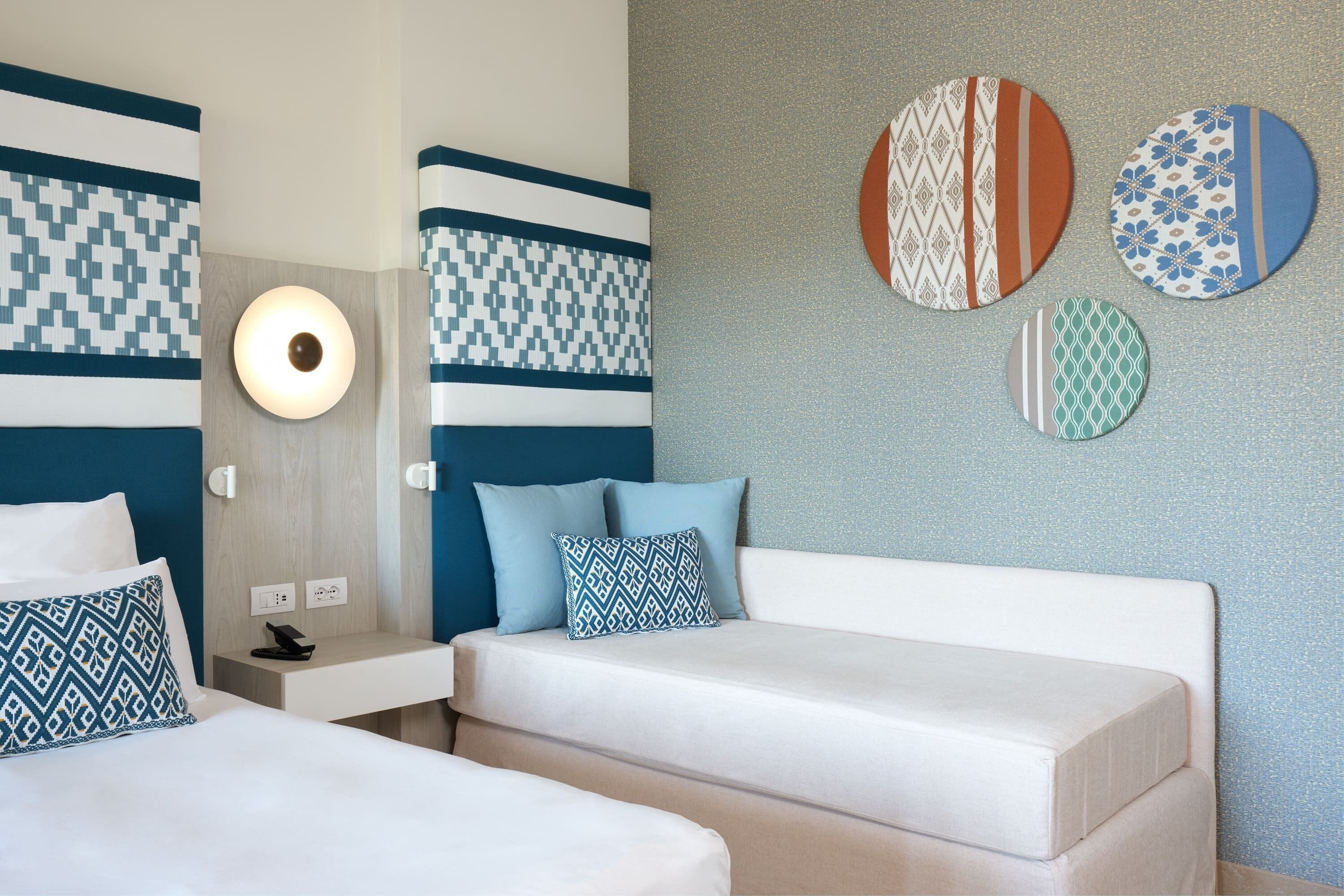 A hotel room with two beds, a bedside table, a wall-mounted light, and decorative wall art.