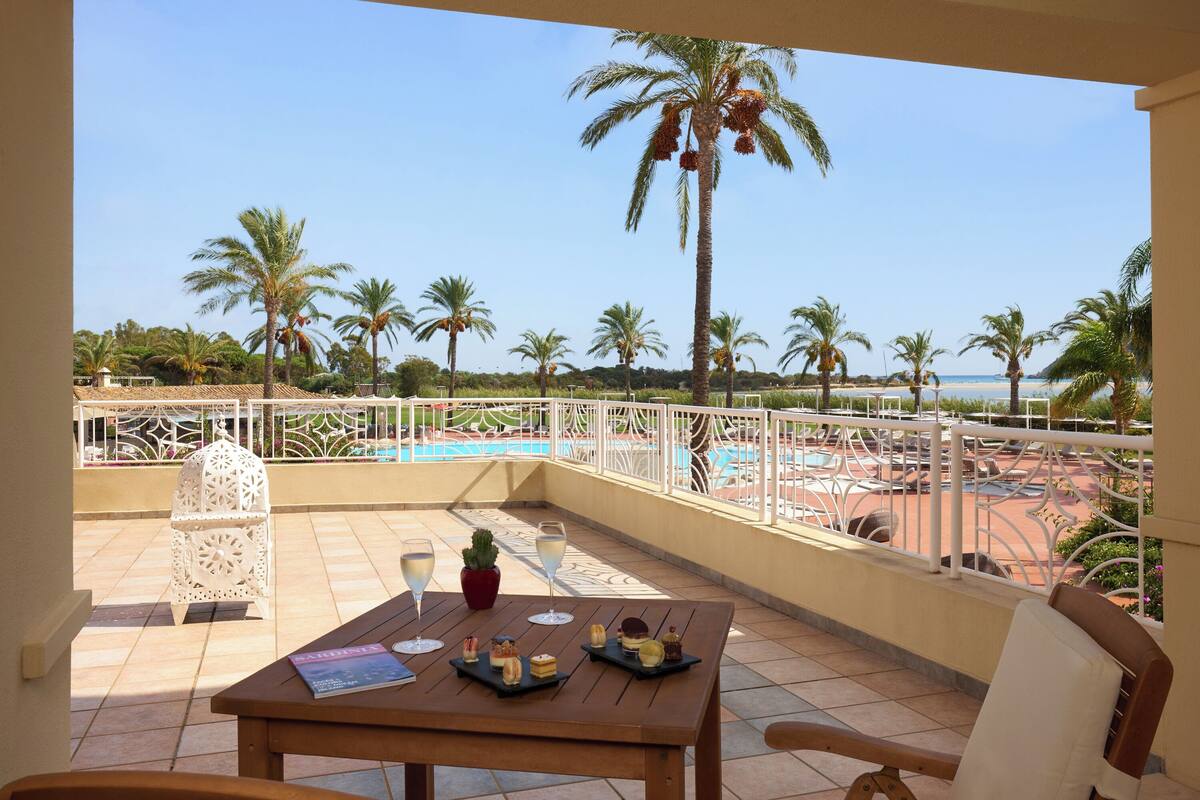 A balcony with a table set for a meal, overlooking a pool and palm trees.