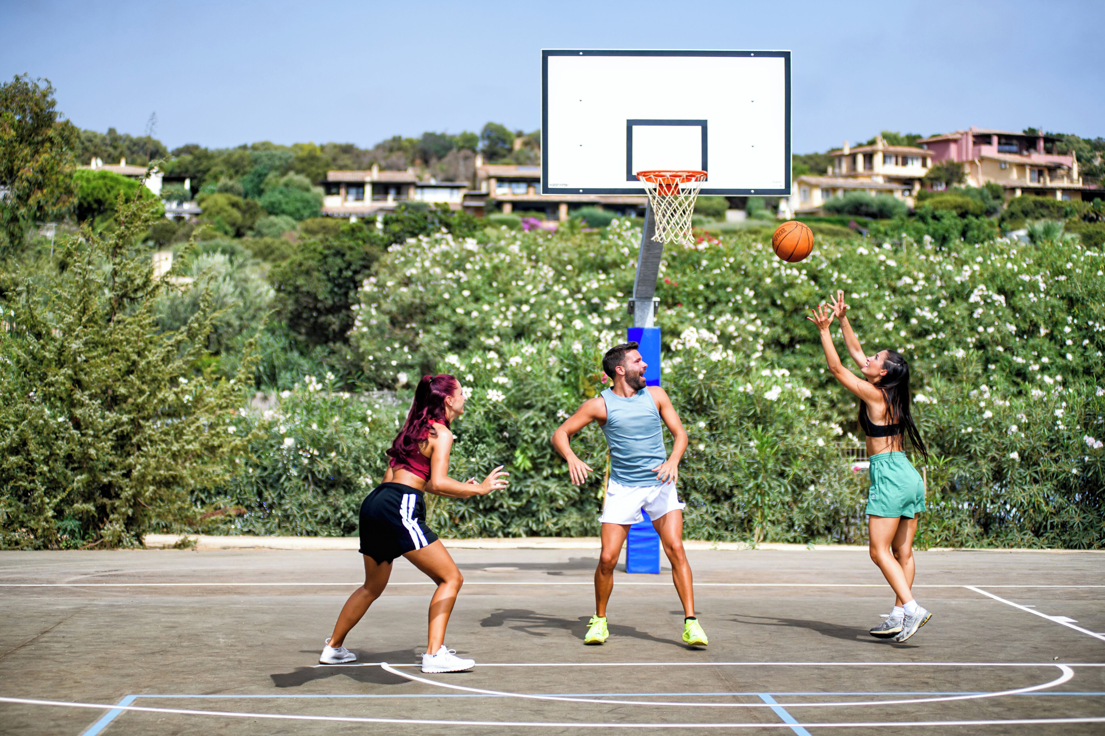 An outdoor basketball court with a hoop and players in motion.