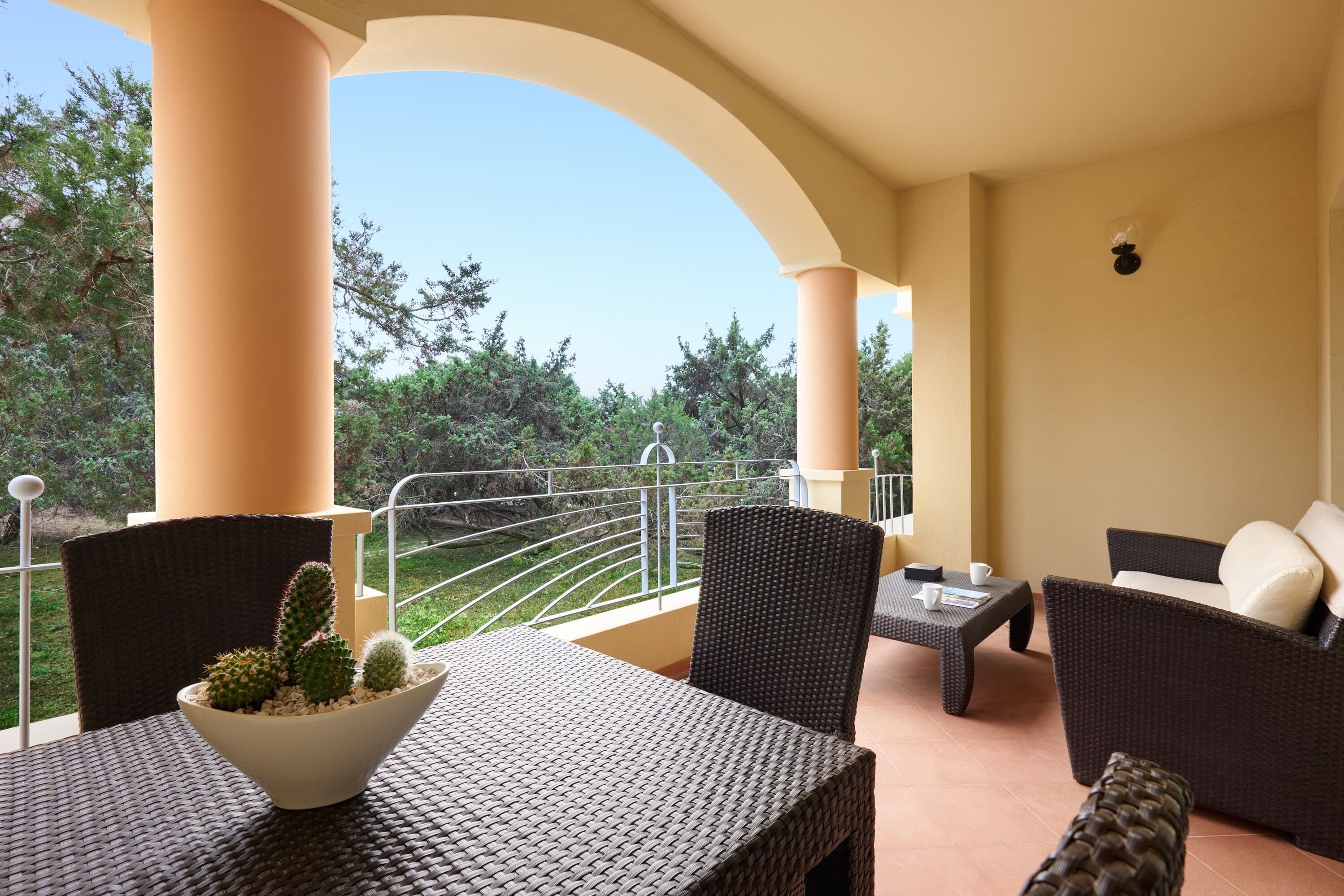 A balcony with wicker furniture, a white table, and a cactus centerpiece.
