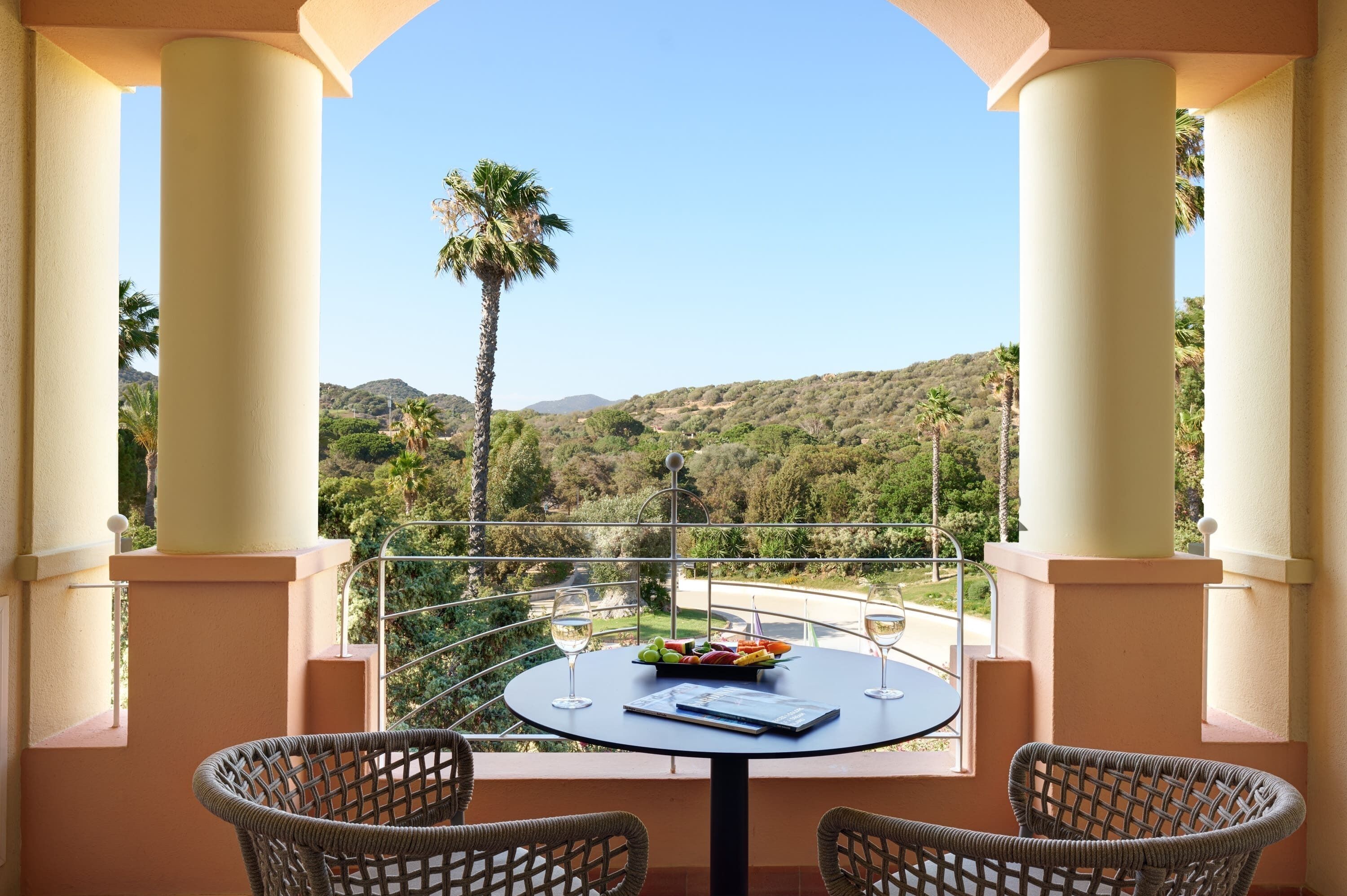 A balcony with a round table, two wicker chairs, and a fruit bowl.