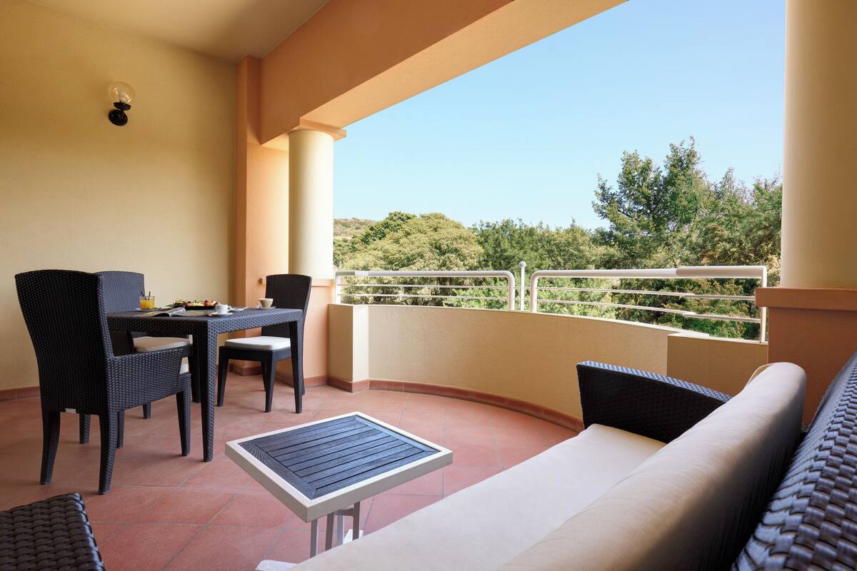 A balcony with a table and chairs, a sofa, and a view of greenery.