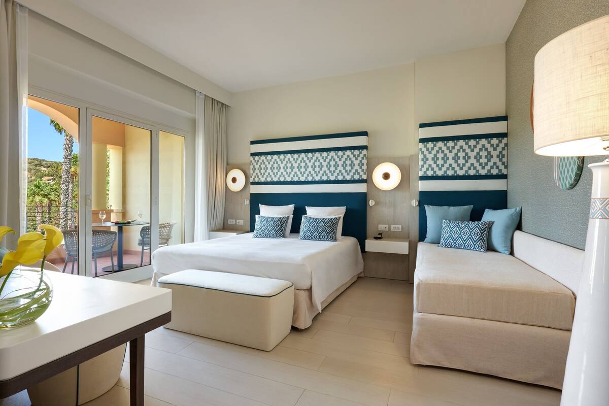 A hotel room with a bed, a sofa, a table, and a view of the outdoors.