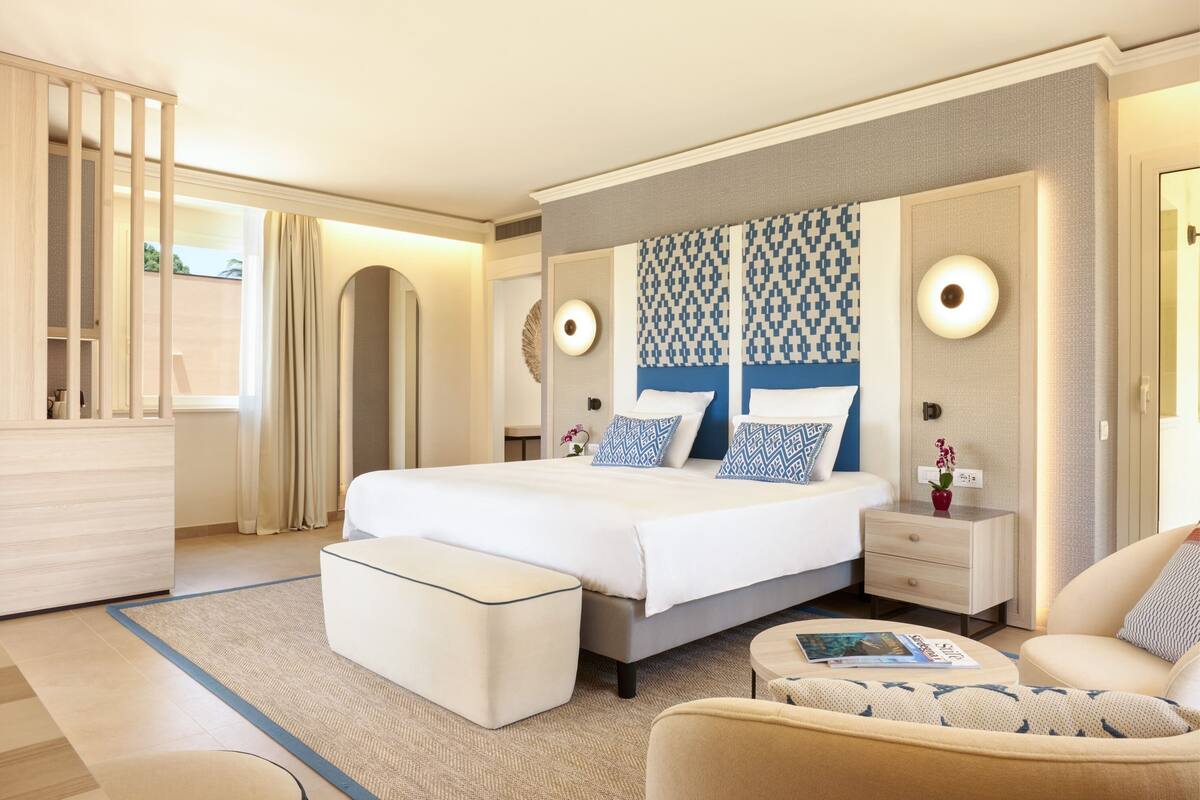 A modern hotel room with a large bed, a bedside table, a nightstand, a sofa, and a small table with a magazine.