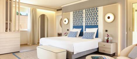 A modern hotel room with a large bed, a bedside table, a nightstand, a sofa, and a small table with a magazine.