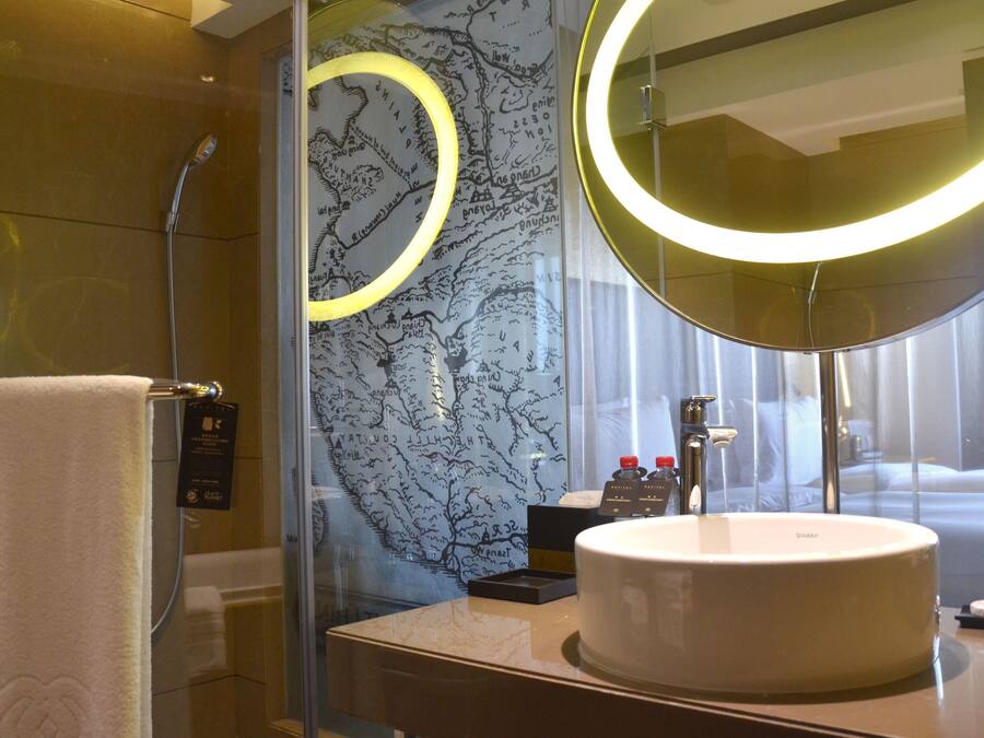 Un baño moderno con un espejo redondo, un lavabo blanco y una ducha con cerramiento de vidrio.