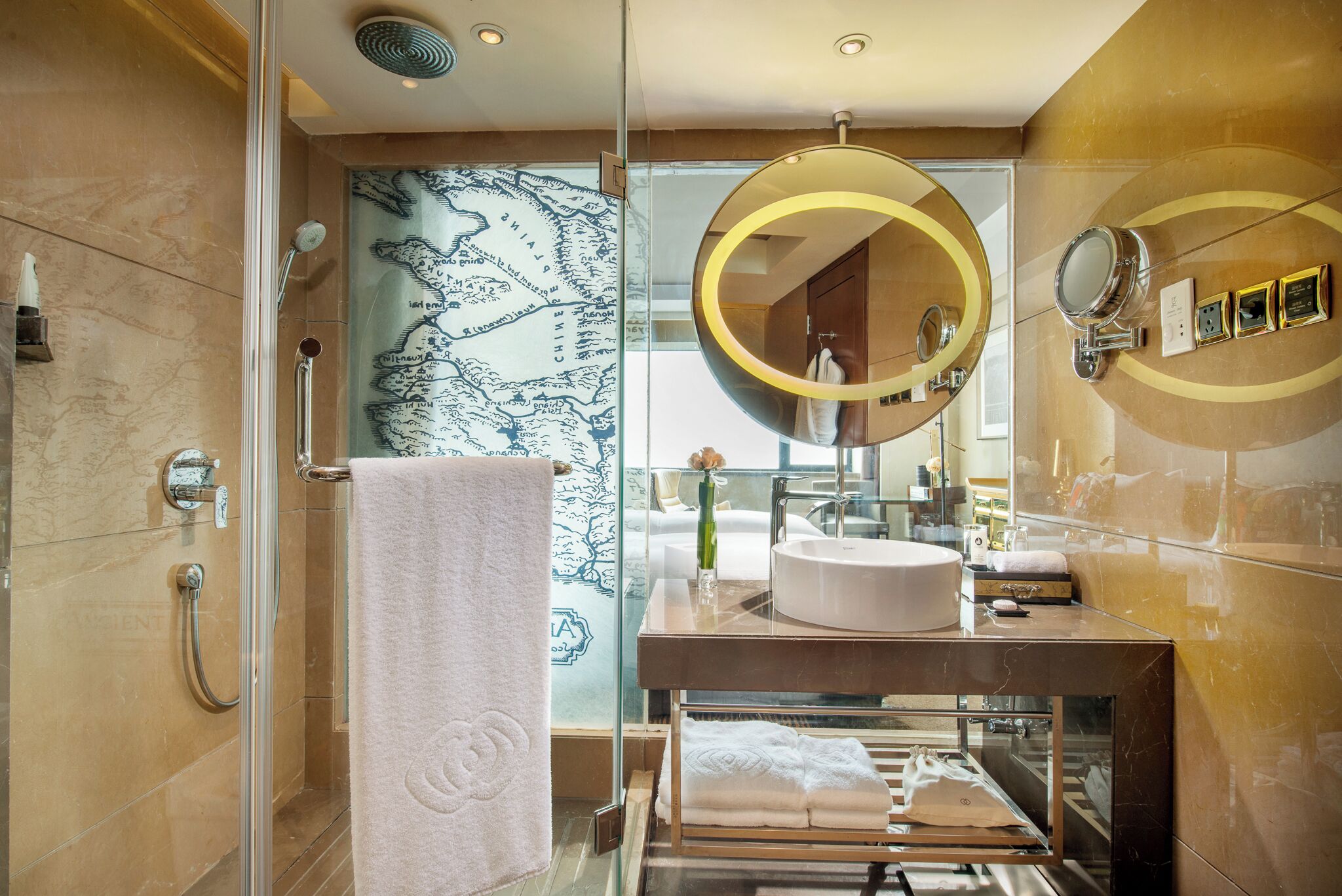 A modern bathroom with a glass shower enclosure, a large round mirror, and a vanity with a sink.