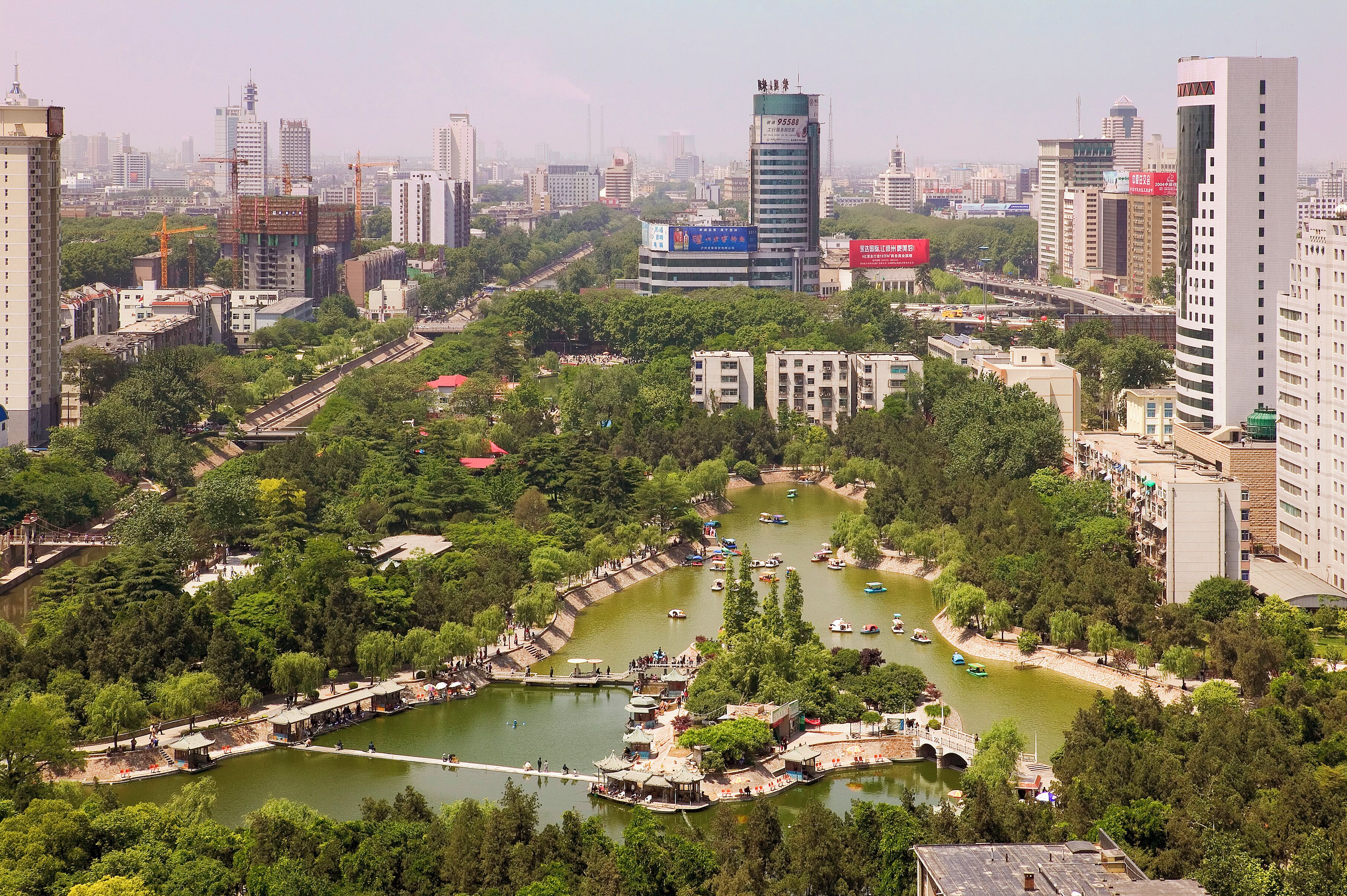 A riverside park with boats, a bridge, and surrounding buildings.